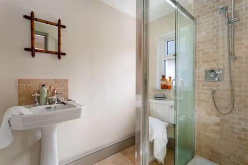 Modern bathroom at 2 Doves Holiday Property, Exeter, with pedestal sink, wood-framed mirror, and walk-in shower enclosure.