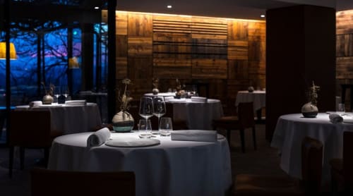Restaurant gastronomique élégant au Clos du Lac avec tables rondes, nappes blanches et vue sur les bois au crépuscule.