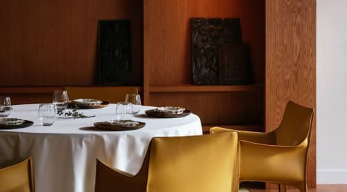 Salle à manger élégante du Clos du Lac avec table ronde, nappe blanche, chaises dorées et niches en bois foncé.