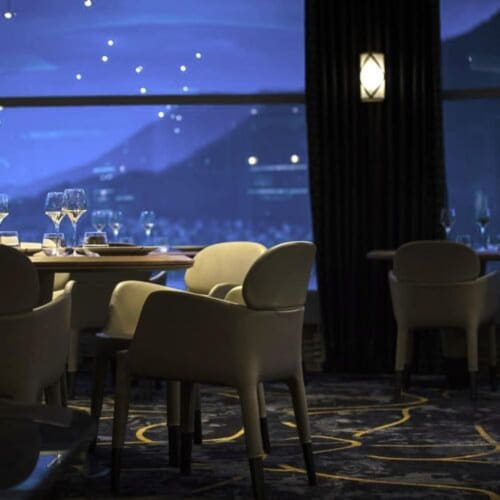 Élégante salle à manger du Clos du Lac avec vue sur le lac, chaises modernes et ambiance tamisée au crépuscule