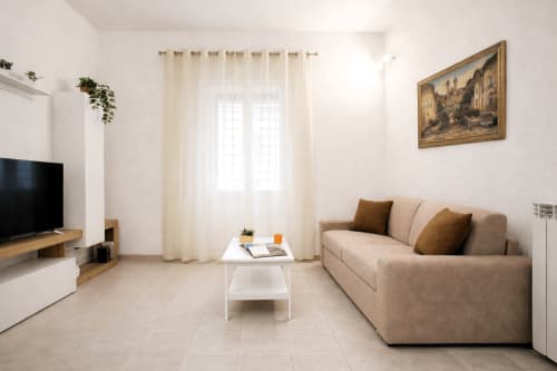Jasny nowoczesny salon w zabytkowym apartamencie w Rzymie z beżową sofą, białym stolikiem do kawy, telewizorem i kremowymi zasłonami