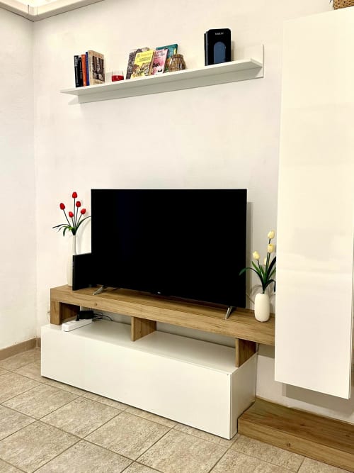 Nowoczesny telewizor w zabytkowym rzymskim apartamencie ze stojakiem drewnianym, białymi półkami, kwiatami ozdobnymi i podłogą wyłożoną płytkami