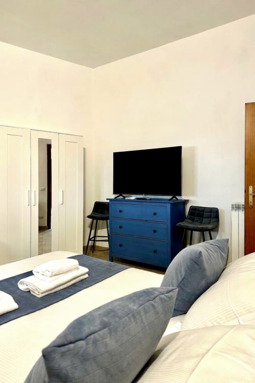 Nowoczesna sypialnia w RomeAntique Stay w Rzymie z niebieską komodą, telewizorem plaskim i wygodnym łóżkiem z poduszkami