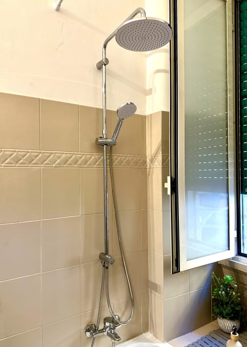 Nowoczesny system prysznicowy z deszczownicą i słuchawką ręczną w łazience wyłożonej beżowymi płytkami w apartamencie RomeAntique Stay w Rzymie