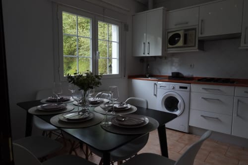 Moderna zona de cocina-comedor en Bizkar Bare Lurra Apartamento 1 con mesa negra, muebles blancos y vistas a la montaña