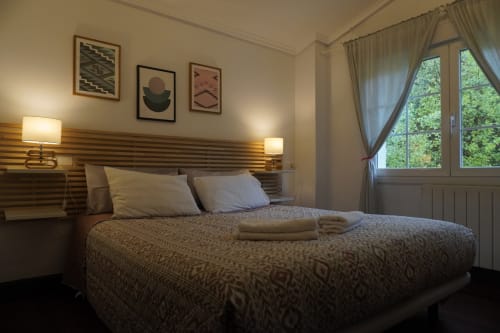 Dormitorio moderno en Bizkar Bare, Vizcaya, con cabecero de madera, iluminación ambiental y vistas a las montañas desde amplios ventanales