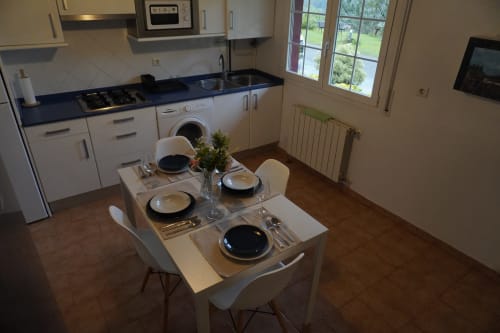Cocina-comedor moderna del apartamento Bizkar Bare con vistas al jardín, muebles blancos y encimeras oscuras
