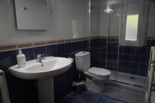 Baño moderno del apartamento Bizkar Bare en Vizcaya con lavabo curvo blanco, inodoro, cabina de ducha y azulejos azul marino