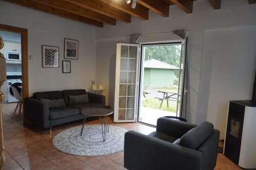 Luminoso salón del apartamento Bizkar Bare en Vizcaya con sofás negros, chimenea y vistas a las montañas por puertas de cristal