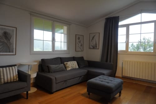 Moderno salón de apartamento en el hotel Bizkar Bare de Vizcaya con sofá negro, vistas a la montaña y pisos de madera