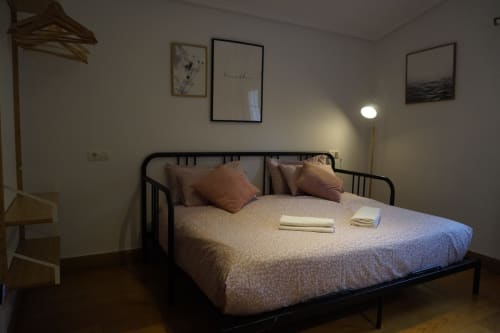 Dormitorio moderno en Bizkar Bare, Vizcaya con cama de estructura negra, almohadas herrumbre y cuadros de montaña