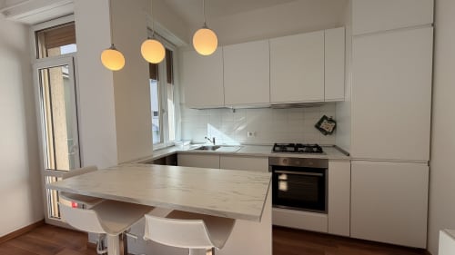Cucina moderna in appartamento AirFlat vicino all'Opera, Milano con cabinetry bianca, isola in marmo, lampade a sospensione e acciaio inox