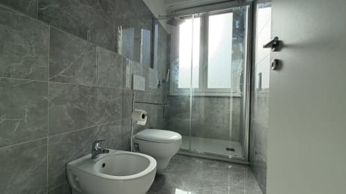 Bagno moderno nell'appartamento Nessa's Home, Opera con piastrelle in marmo grigio, bidet, WC e cabina doccia in vetro