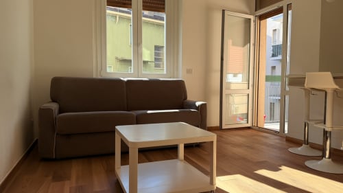 Moderno salotto in Opera con divano marrone, tavolo in legno e vista sul balcone - Nessa's Home di AirFlat