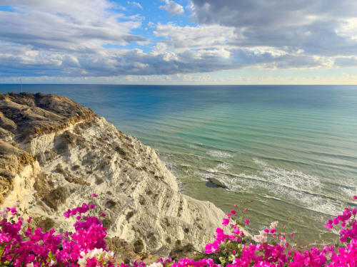 Magenta flowers frame white cliffs overlooking turquoise sea near Stella del Mare, Licata, Sicily