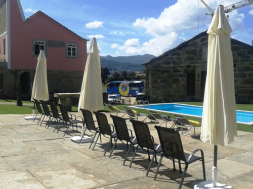 Área de descanso à beira da piscina da Quinta de Anterronde com guarda-sóis, espreguiçadeiras e vista para as montanhas em Arouca, Portugal