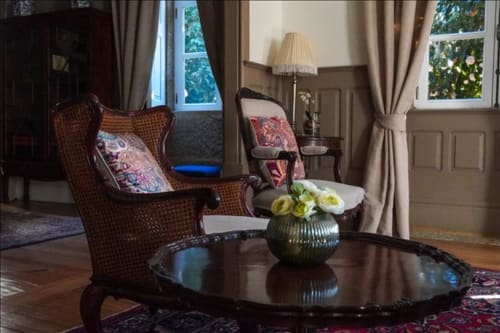 Elegante sala de estar na Quinta de Anterronde, Arouca com poltronas de vime, mesa redonda escura com arranjo floral, e