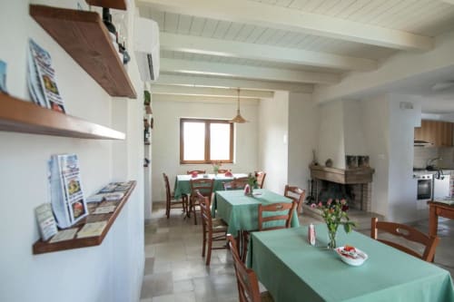 Luminosa sala da pranzo al Trulli Boccadoro B&B con tovaglie verdi, sedie in legno, soffitto con travi bianche e accesso alla cucina.