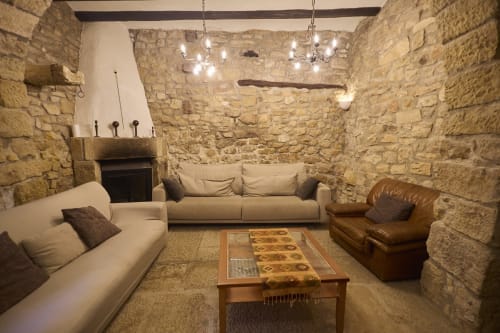 Habitación rústica de piedra en RuralGorgs B&B, El Vilosell, con sofás crema, sillón de cuero, mesa de madera y lámparas de araña modernas