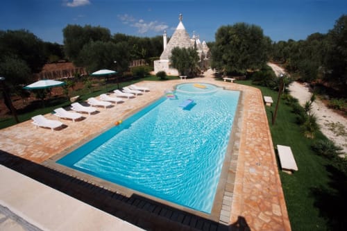 Piscina del Trulli Boccadoro B&B in Italia con lettini, caratteristici trulli a forma conica, ulivi e cielo azzurro limpido