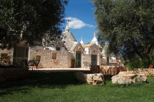 Bed and breakfast Trulli Boccadoro in Italia con tradizionali costruzioni in pietra, prato verde e ulivi sotto cielo sereno