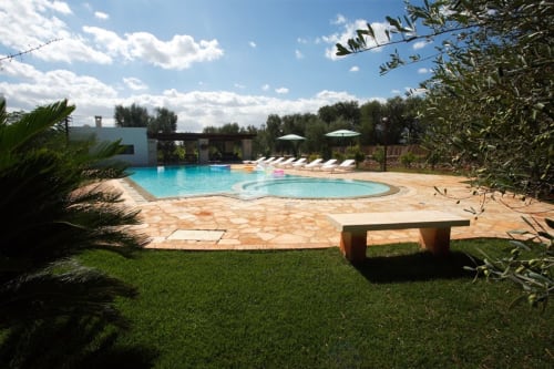 Area piscina di Trulli Boccadoro con lettini, ombrelloni e patio in pietra circondato da ulivi