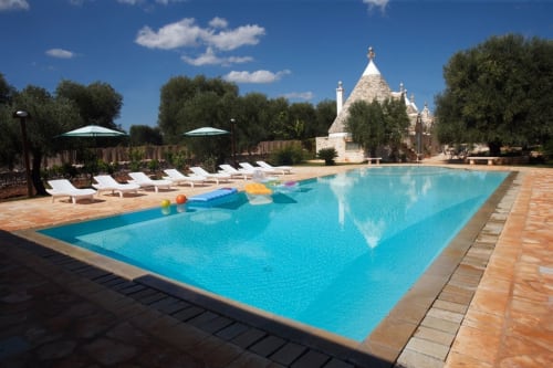 Piscina turchese a Trulli Boccadoro con lettini, ombrelloni e l'architettura tradizionale dei trulli sullo sfondo