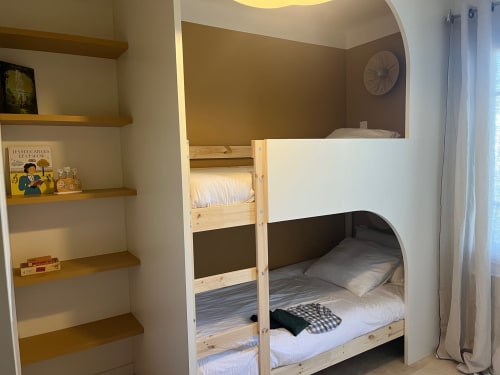 Chambre de la villa Mas de Lucienne avec lits superposés en bois, literie blanche, étagères murales avec livres et décorations, horloge