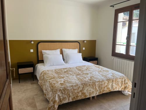 Chambre moderne de la villa Soleù Mas de Lucienne avec mur d'accent moutarde, tête de lit en rotin, draps blancs et portes-fenêtres