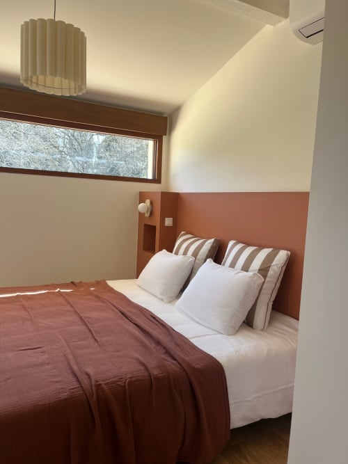 Chambre moderne à la villa Soleù Mas de Lucienne avec mur d'accent en terre cuite, literie blanche, coussins rayés et vue sur le jardin