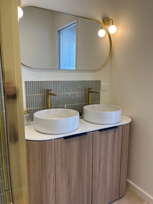 Salle de bain moderne à la villa Soleù avec doubles vasques blanches, vanité aux formes arrondies, robinetterie en laiton et miroir rond rétroéclairé