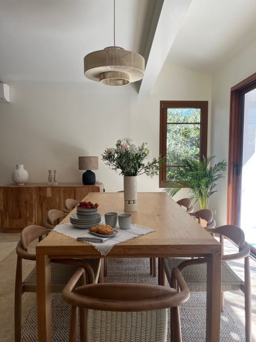 Salle à manger de la villa Soleù Mas de Lucienne avec table en bois, luminaire suspendu moderne et vue sur le jardin par les portes-fenêtres
