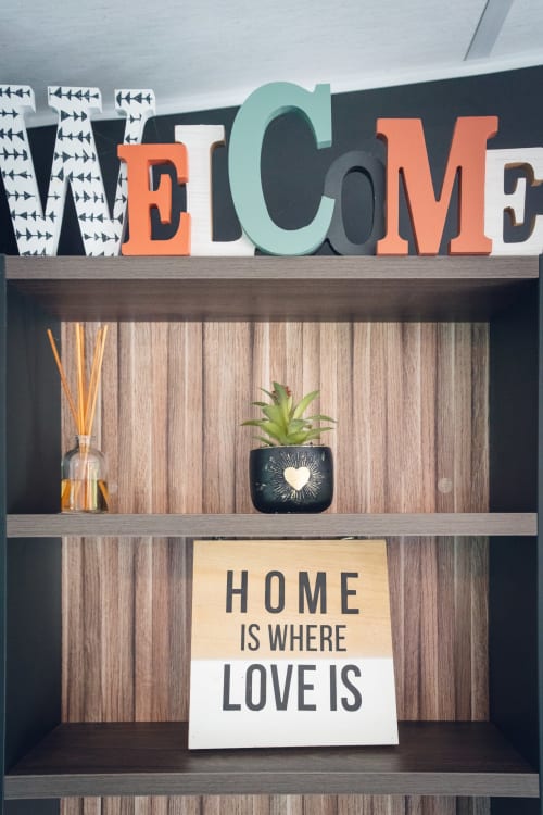 Étagère d'accueil avec panneau « WELCOME », plante succulente, diffuseur de roseaux et citation « Home is Where Love is » au Maquis