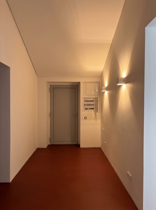 Corredor moderno da villa Casa Igrejinha com iluminação acolhedora, piso vermelho, paredes brancas e porta de entrada na casa de hóspedes Alentejo33