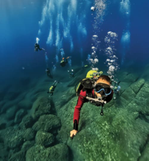 Scuba divers exploring underwater rock formations near Muravera, Italy