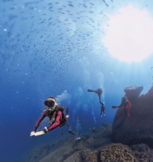 Scuba divers exploring underwater rock formations in clear blue Mediterranean waters near Muravera, Italy