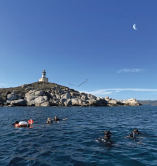 Crewed boat near rocky island with lighthouse off Muravera coast, Italy