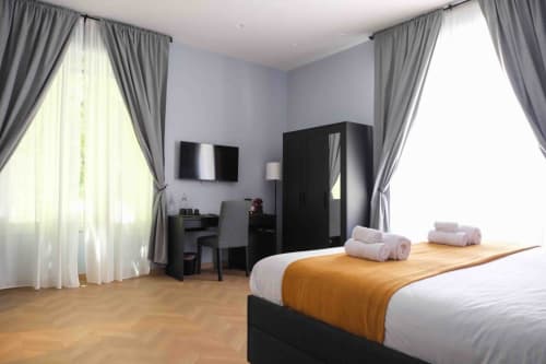Lussuosa camera matrimoniale presso Mazzini Suites Palermo con letto, arredamento nero, pavimento in legno e tende grigie