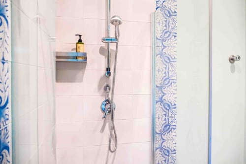 Bagno moderno alle Mazzini Suites Palermo con piastrelle rosa, soffione pioggia, dettagli blu e dispenser di sapone