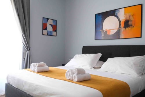 Lussuosa camera da letto matrimoniale alle Mazzini Suites Palermo con biancheria bianca, testata nera e opere d'arte moderna a Palermo, Italia
