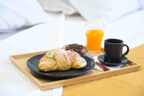 Vassoio colazione alle Mazzini Suites Palermo con cornetto, caffè, succo e pasticcini su tavolo in legno