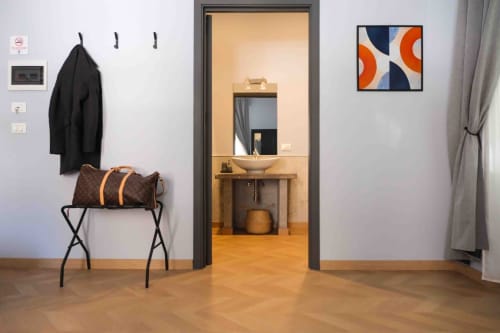 Ingresso della suite di lusso Mazzini Suites Palermo con cappotto nero, valigia marrone e opere d'arte moderna