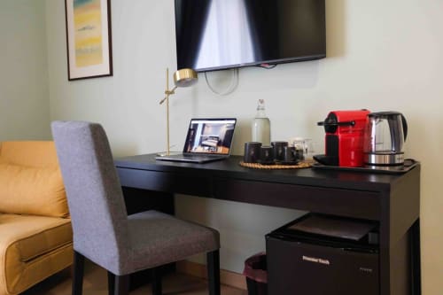 Scrivania moderna di Mazzini Suites Palermo con laptop, macchinetta caffè rossa e TV a parete in camera di lusso