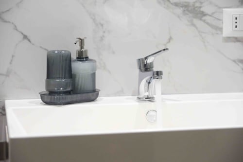 Modern bathroom sink with chrome faucet and gray soap dispenser at Mazzini Suites Palermo, marble backsplash