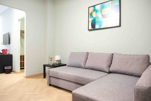 Modern living area with gray sectional sofa at Mazzini Suites Palermo, featuring wooden floors and wall art