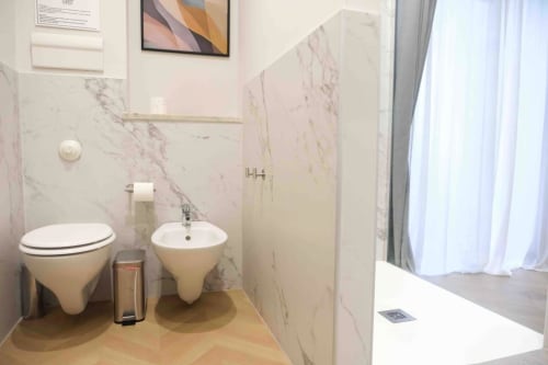 Bagno moderno delle Mazzini Suites Palermo con pareti in marmo, wc e bidet sospesi, e cabina doccia in vetro
