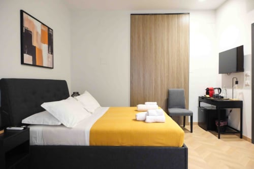 Modern bedroom at Mazzini Suites Palermo with black bed, yellow blanket, and wood-slat accent wall