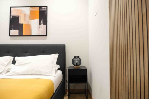 Camera moderna delle Mazzini Suites Palermo con testata nera, cuscini bianchi, coperta gialla, arte astratta e tende