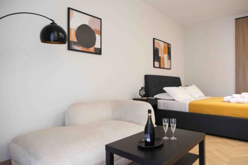 Camera moderna delle Mazzini Suites Palermo con letto nero, poltrona color crema, lampada ad arco e opera d'arte astratta