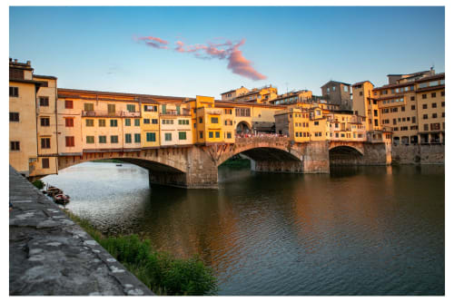 Ponte Vecchio bridge spanning the Arno River in Florence with golden Renaissance buildings and clear blue sky